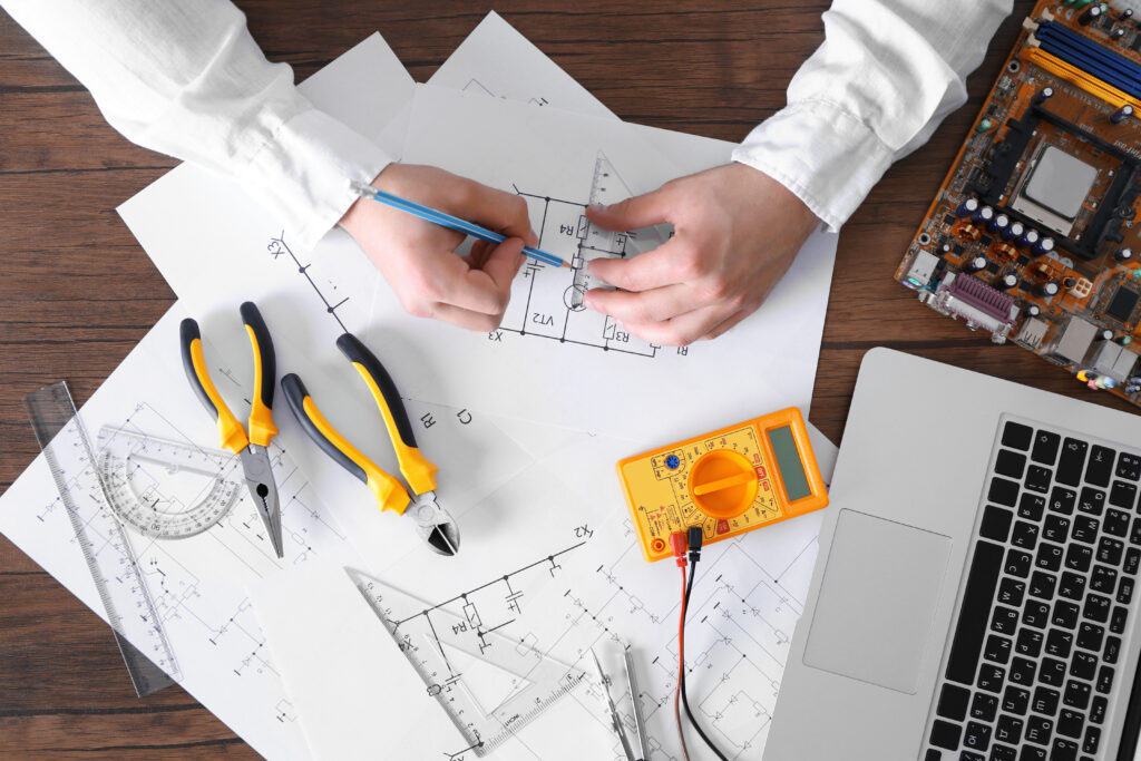 Male hands drawing electrical blueprint at wooden table, top view